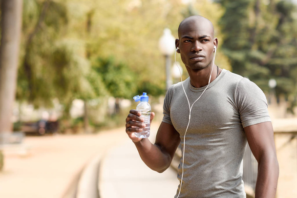 Jovem negro bebendo água antes de correr em backgroun urbano
 - Foto, Imagem