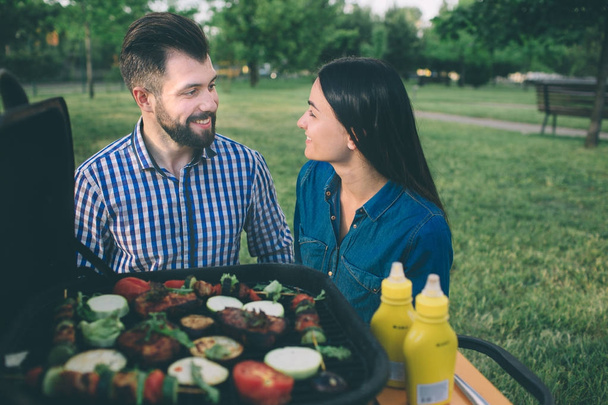 Amis faisant barbecue et déjeuner dans la nature. Couple s'amuser tout en mangeant et en buvant à un pic-nic - Les gens heureux à la fête bbq
. - Photo, image
