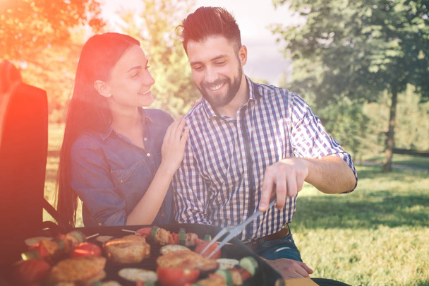 Friends making barbecue and having lunch in the nature. Couple having fun while eating and drinking at a pic-nic - Happy people at bbq party. - Foto, Imagen
