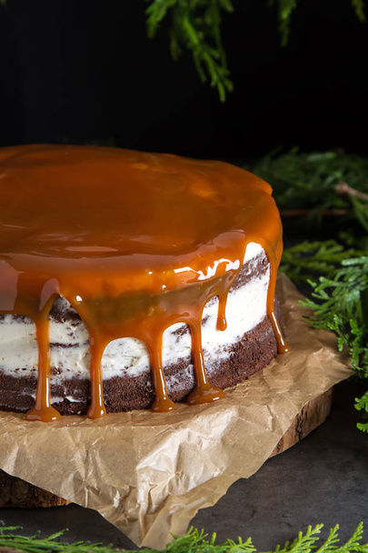 Chocolate cake with white cream and caramel sauce. Dark background. Birthday - 写真・画像
