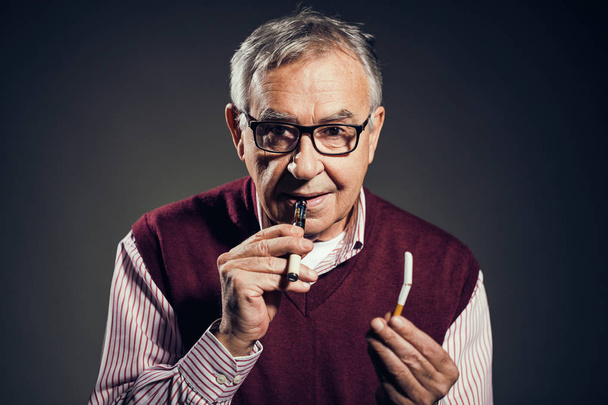 Portret starszego człowieka, który postanowił rzucić palenie papierosów na rzecz elektronicznego papierosa.  - Zdjęcie, obraz