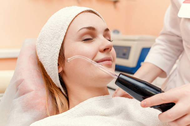 Mujer joven en el procedimiento de masaje facial darsonval eléctrico en el salón de belleza
. - Foto, Imagen