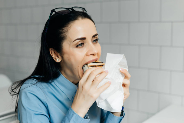 молодая голодная брюнетка студентка завтракает в кафе с бутербродом и кофе
 - Фото, изображение