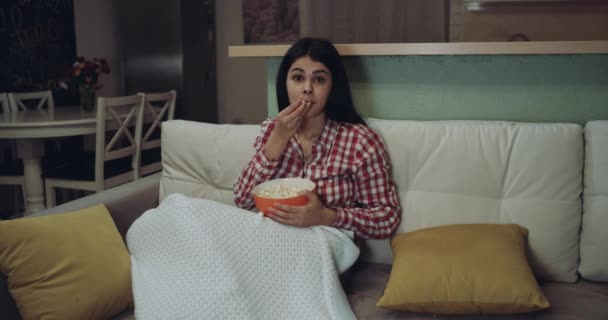 Young woman watching tv eating the popcorn and is very excited. - Imágenes, Vídeo