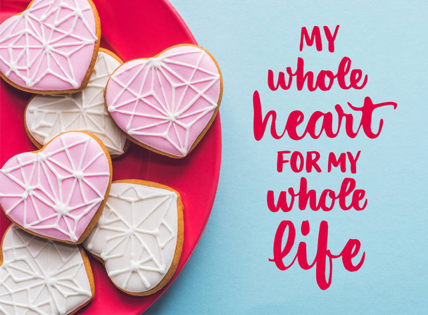 top view of glazed heart shaped cookies on pink plate isolated on blue - Foto, Bild