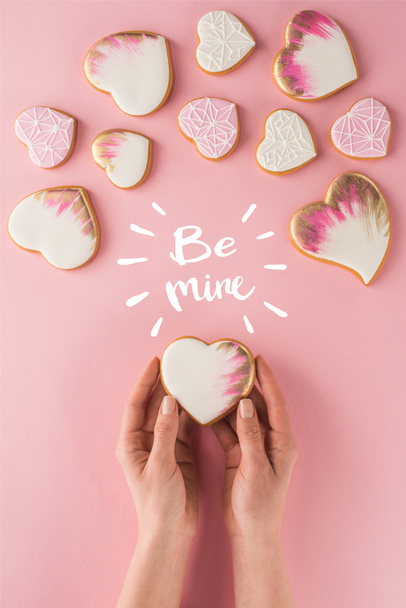 partial view of woman holding glazed cookie in hands isolated on pink, st valentines day concept - 写真・画像