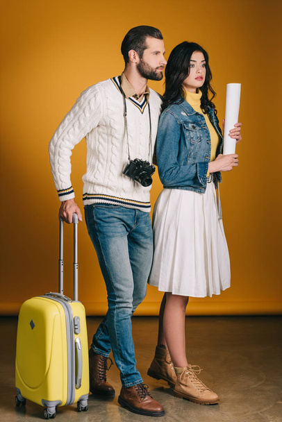 travelers with bag on wheels looking away on yellow - Фото, зображення