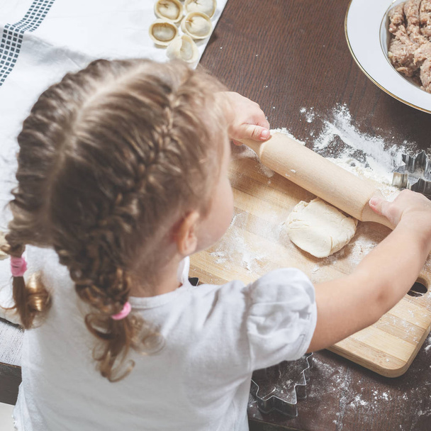 Mała dziewczynka rolkach ciasta za pomocą drewnianym wałkiem - Zdjęcie, obraz