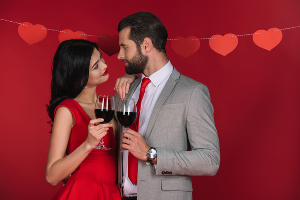 couple with wineglasses looking at each other isolated on red - Photo, Image