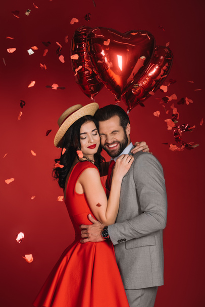 laughing couple under falling confetti isolated on red - Foto, Bild