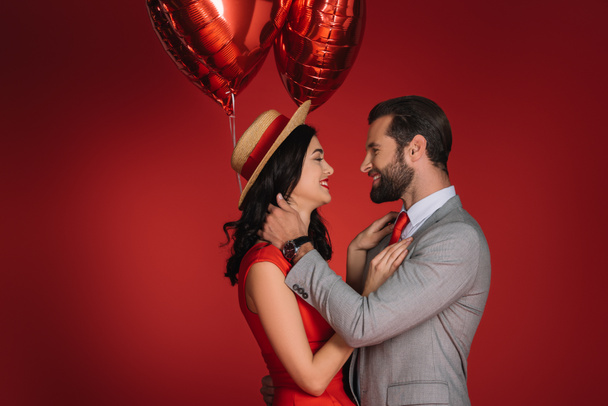 pareja elegante con globos rojos mirándose aislados en rojo
 - Foto, Imagen