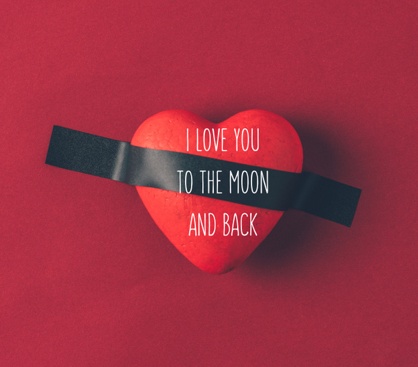 Top view of red heart under insulating tape with words i love you to the moon and back on red
 - Фото, изображение