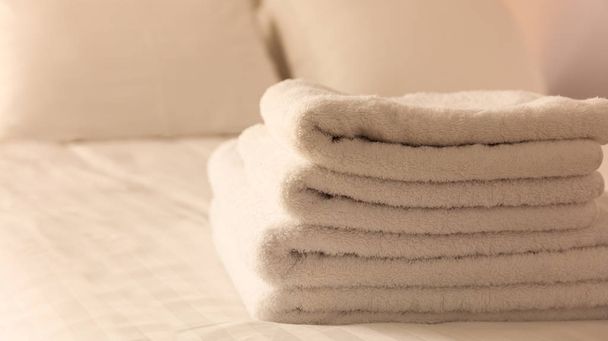 Hotel bedroom. White fluffy, folded towels, linen sheets and pillows on bed. Close up view. - Photo, Image