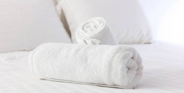 La habitación del hotel. Blanco esponjoso, toallas enrolladas, sábanas de lino y almohadas en una cama. Vista de cerca
. - Foto, Imagen