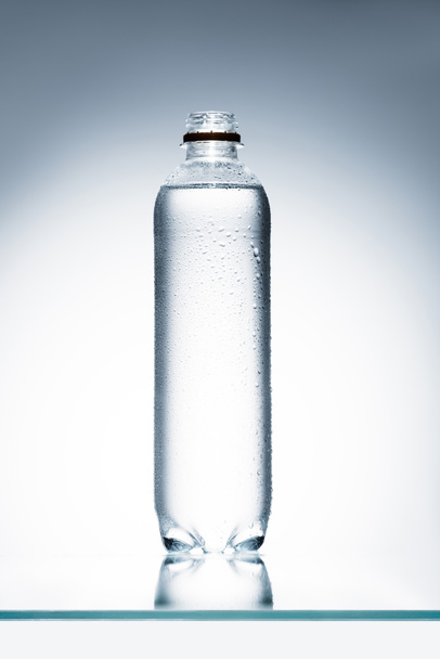 botella de plástico llena de agua en la superficie reflectante
 - Foto, imagen
