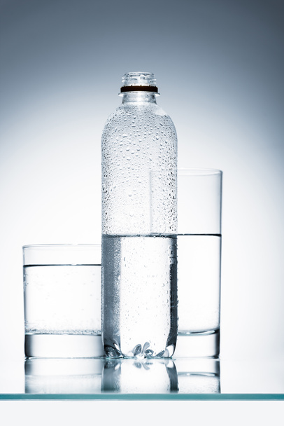 plastic bottle and glasses of clean water on reflective surface - Foto, Imagem