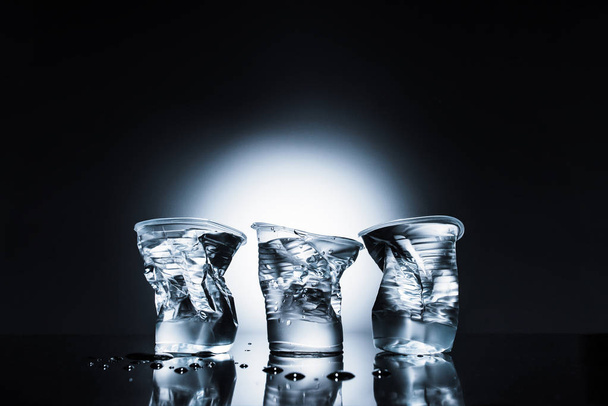 τσαλακωμένο πλαστικά ποτήρια νερού στο σκοτάδι  - Φωτογραφία, εικόνα