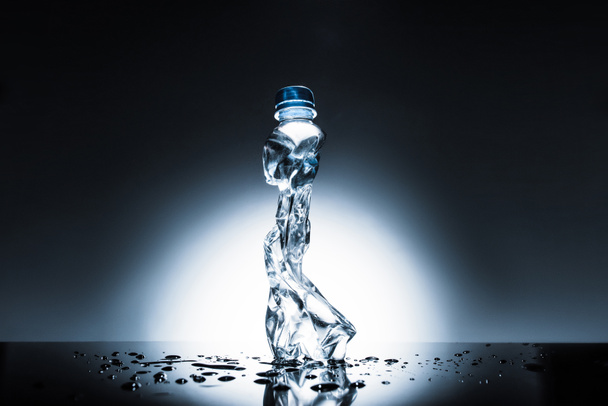zerknüllte Plastikflasche mit Wasser auf dunklem  - Foto, Bild