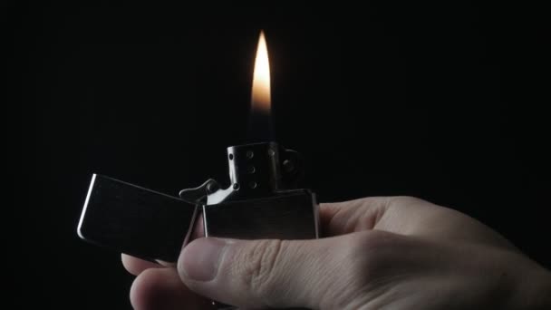 Nahaufnahme der Öffnung und des Verbrennens von eisernem Reißverschlussfeuerzeug auf schwarzem Hintergrund - Filmmaterial, Video