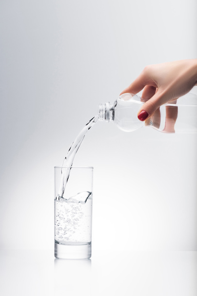 プラスチック ボトルからグラスに水を注ぐ女性のショットをトリミング - 写真・画像