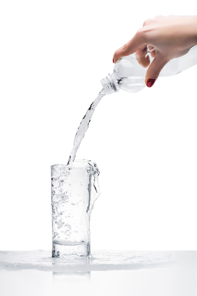 白で隔離プラスチック ボトルからグラスに水を注ぐ女性のクロップ撮影 - 写真・画像