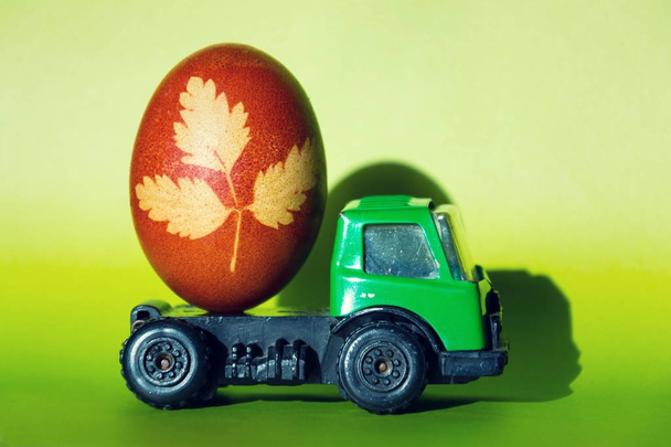 Hierba de Pascua marrón-roja decorada huevo coloreado con infusión de cebolla en coche de juguete verde aislado en fondo fresco filtrado vintage
 - Foto, Imagen