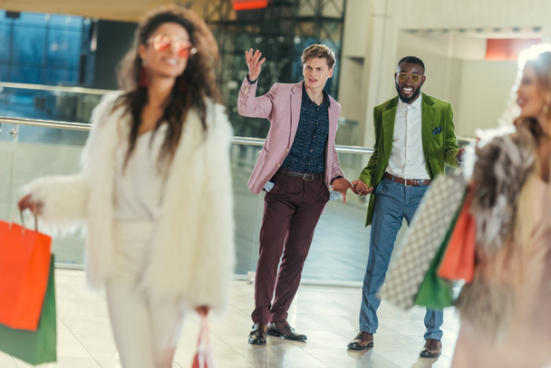 stylish women with shopping bags walking away from shocked boyfriends with empty pockets - Fotografie, Obrázek