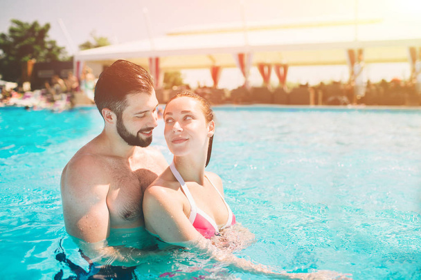 Cheerful youthful guy and lady resting while swimming pool outdoor. Couple in water. Guys do summer sephi - 写真・画像