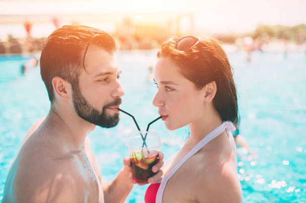 Young couple by the swimming pool. Man and women drinking cocktails in the water - Φωτογραφία, εικόνα