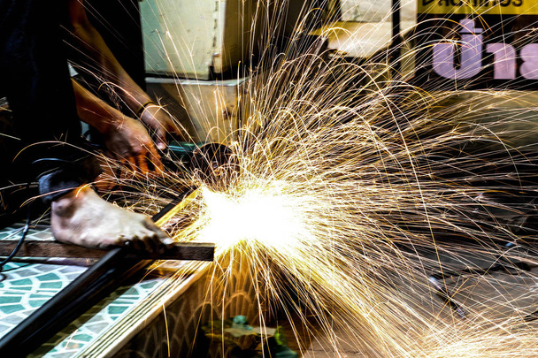  Рабочий режет металл дробилкой. Искры во время шлифования железа - Фото, изображение