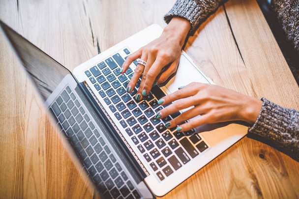 Close-up da mão de uma jovem em uma camisola cinza usar tecnologia laptop em uma mesa de madeira em um café. Perto do telemóvel e dos óculos. O conceito de senhora de negócios de trabalho remoto
. - Foto, Imagem