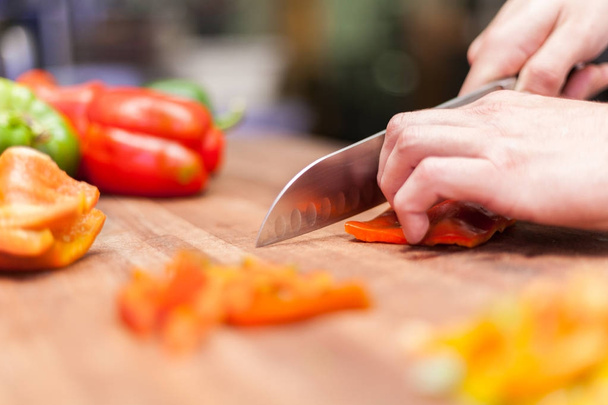 koken. Close up van mannenhand snijden peper op snijplank thuis - Foto, afbeelding