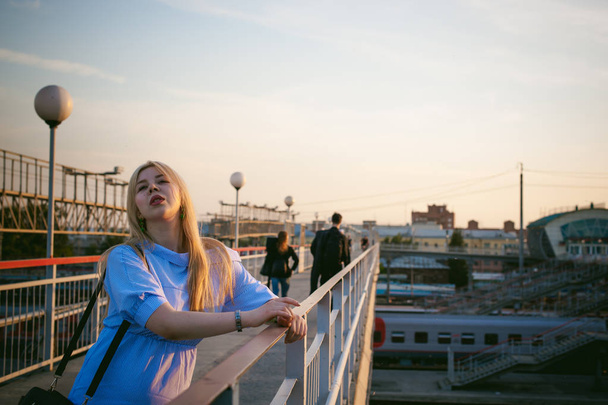 portrait of a cute young blond woman in a summer day against the background of a railway station - Фото, зображення
