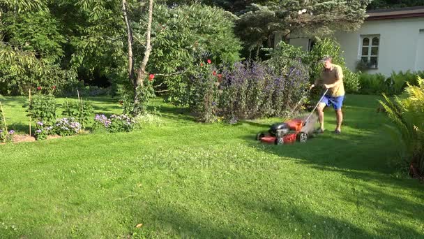 Miespuutarhuri työntää ruohonleikkuria talonsa pihalla. 4K
 - Materiaali, video