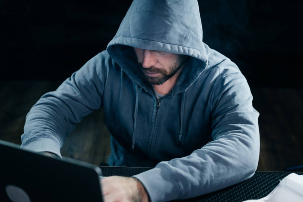 mysterious bearded man in a hood doing something illegal on a laptop - 写真・画像