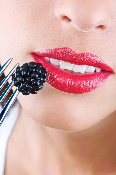 Mouth of a young woman and an appetizing blackberry. Icon of healthy eating. - Photo, Image