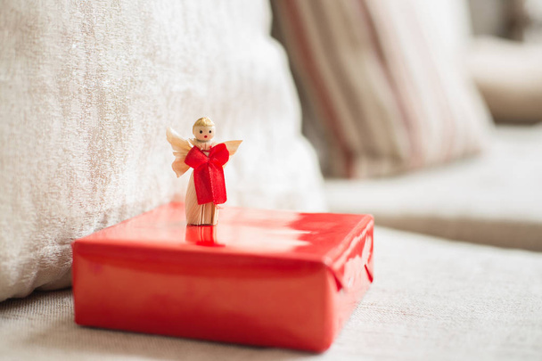 a gift packed with red paper and a figure of an angel with red ribbon left on a couch - Photo, Image
