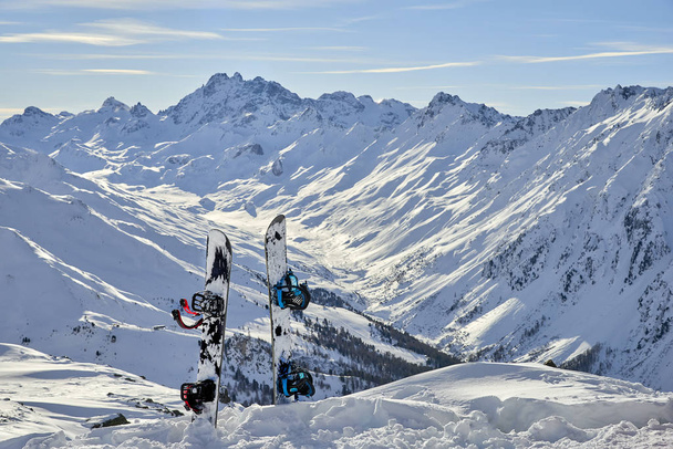 Snowboard en nieve en pendiente fuera de pista en el día del sol entre montañas en el fondo
 - Foto, Imagen