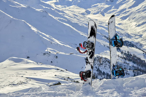 Dos tablas de snowboard de pie en la nieve entre montañas en el fondo
 - Foto, Imagen