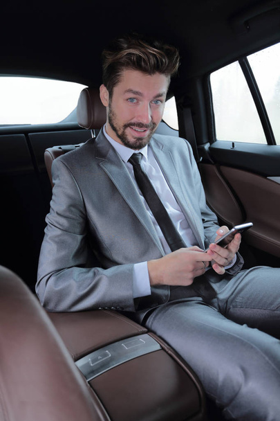 man in suit sitting in car and reading messages on smartphone - Photo, image