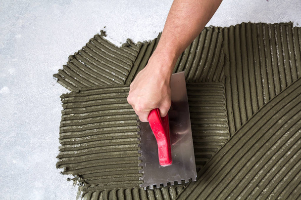 Рабочая рука с лопатой инструмент для установки плитки делает Morta
 - Фото, изображение