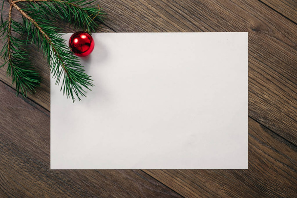 A frame of pine branches and Christmas decorations and A4 sheet of white paper on a wooden table. Holidays christmas background. Copy space for text or design. View from above. - Photo, Image