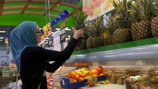 Muslim girl shopping, selects fresh pineapples - Video, Çekim