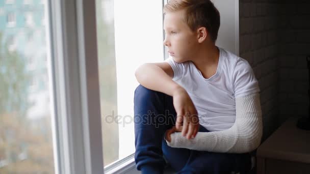 Θλιβερή αγόρι με σπασμένο χέρι που βλέπουν το παράθυρο - Πλάνα, βίντεο