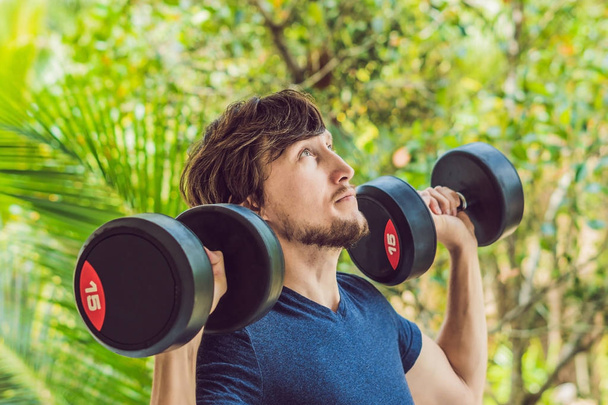 Training fitness man outside working out arms lifting dumbbells doing biceps curls. Male sports model exercising outdoors as part of healthy lifestyle. - Foto, afbeelding