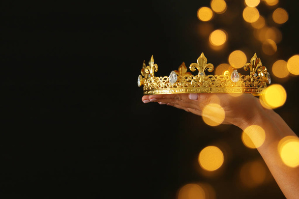 Woman's hand holding a crown for show victory or winning first place over black background with glitter overlay. - Foto, immagini