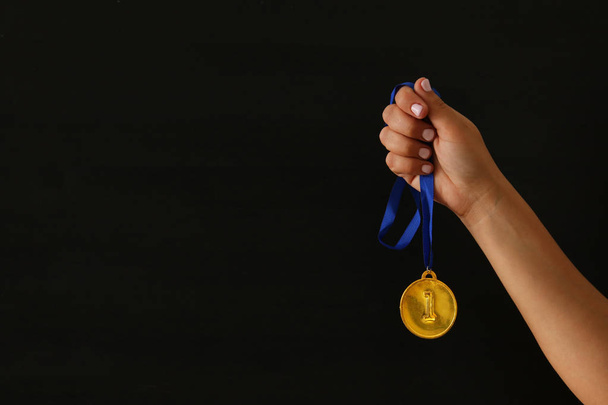 Ženská ruka držící zlatou medaili proti černému pozadí. Ocenění a vítězství koncept. - Fotografie, Obrázek
