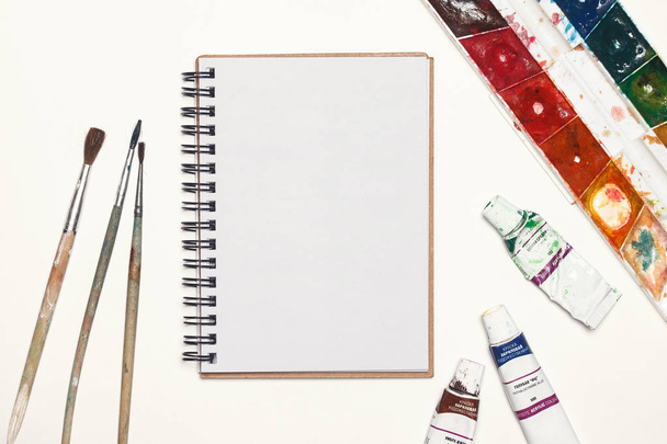 Notebook mock up for artwork with watercolor paints, palette and a paintbrushes. Top view. Artistic work tools on white background. - Фото, зображення