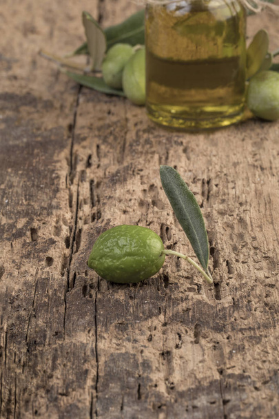 Onrijpe groene olijven en olijfolie op houten tafel - Foto, afbeelding