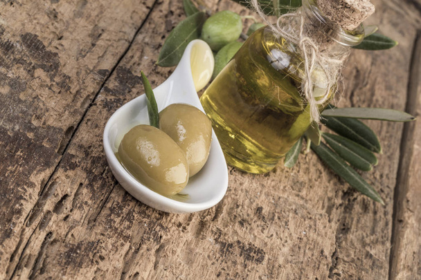 Green olives and olive oil on wooden table - Foto, afbeelding